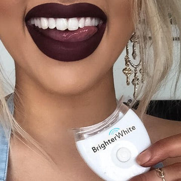 Smiling woman with dark lipstick holding a BrighterWhite LED accelerator light