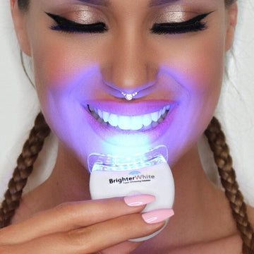 Smiling woman using the BrighterWhite LED accelerator light, its blue-violet glow lighting up her teeth