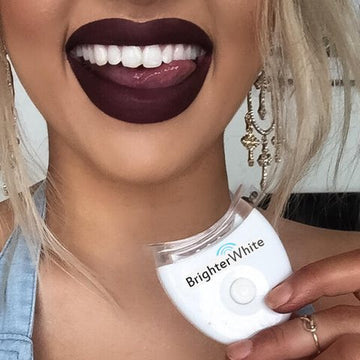 Smiling woman with dark lipstick holding a BrighterWhite LED accelerator light